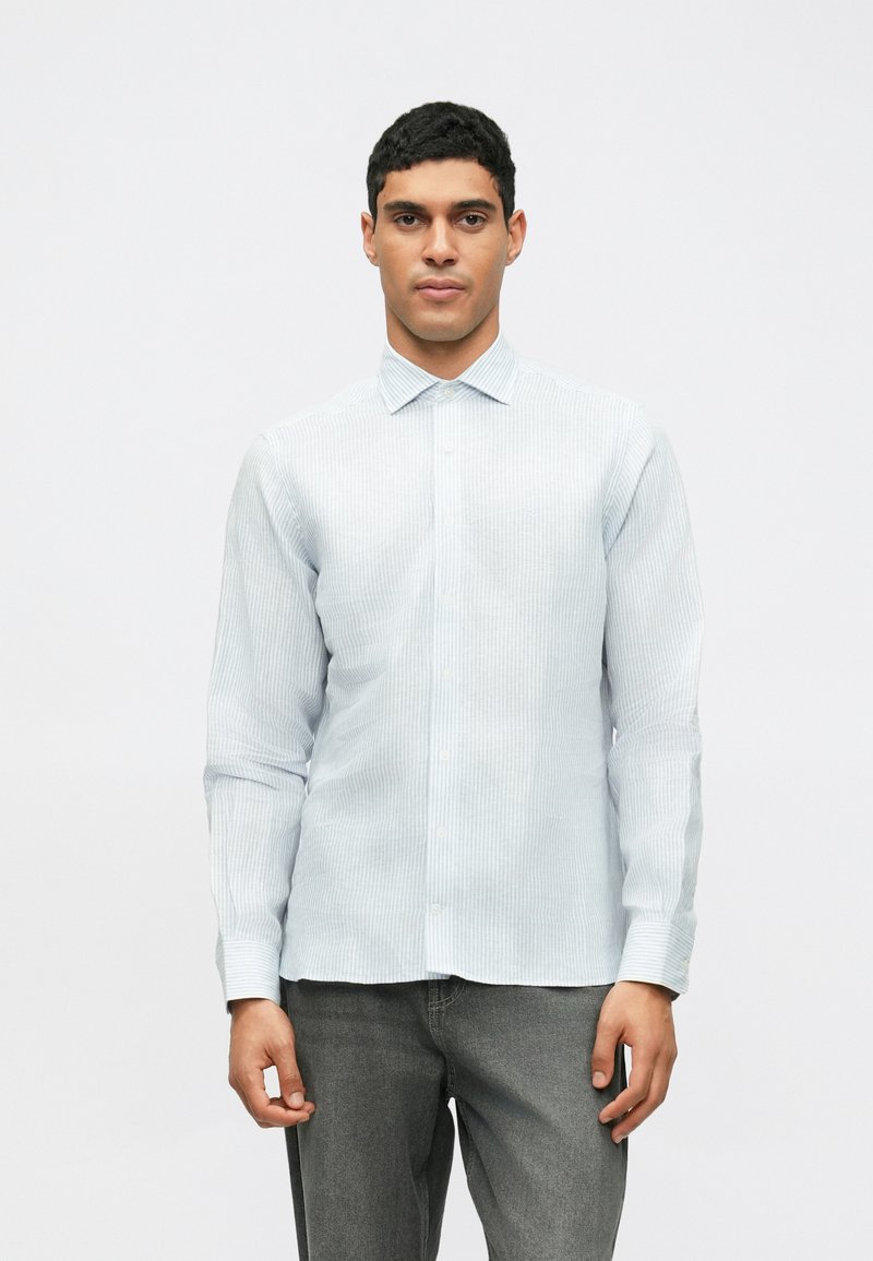 Világoskék, hosszúujjú ing, finom csíkokkal, gombos záródással és hegyes gallérral. Az anyag sima kinézetű, laza szabással.