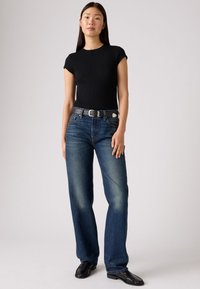 Juoda trumpomis rankovėmis megzta viršutinė dalis, mėlyni tiesūs džinsai su subtiliu nudėvėjimu, pilkas diržas su sidabrine sagtimi ir juodi loaferiai.