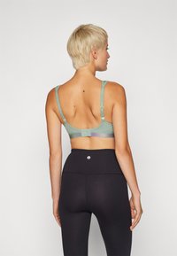 Sujetador verde claro con tirantes ajustables, tejido texturizado y cierre de gancho. Presenta una banda de acento multicolor en la parte posterior.