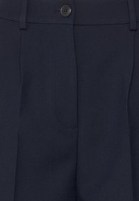Pantaloni su misura blu navy in tessuto morbido, con chiusura a un bottone e pince frontali. Presentano dettagli di cucitura discreti.