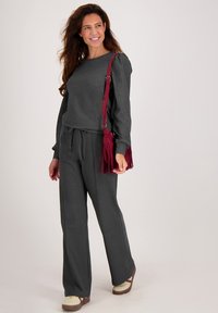 Grijze trui en bijpassende broek met een relaxte pasvorm en een trekkoord in de taille. Gecombineerd met een bordeauxrode franjerugzak en meerkleurige sneakers.