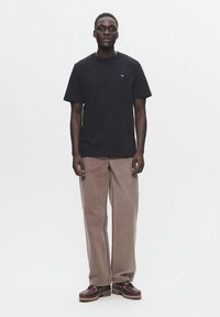 Μαύρο βαμβακερό T-shirt με στρογγυλή λαιμόκοψη και κοντά μανίκια, συνδυασμένο με ανοιχτό καφέ παντελόνι με φαρδιές παντελόνες και σκούρα καφέ μποτάκια με κορδόνια.