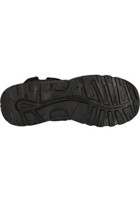 Svart gummisula med ett robust mönster, breda spår och en slät mittlinje. Detaljer med kardborreband är synliga.