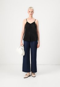 Svart, plissert camisetttopp, brede mørkeblå jeans, beige flate sko og en hvit håndveske. Enkle linjer og kontrasterende farger.