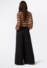Mehrfarbige Bluse mit Zickzackmuster und Puffärmeln, kombiniert mit hochgeschnittenen, schwarzen weit geschnittenen Hosen. Glatte Stoffstruktur.