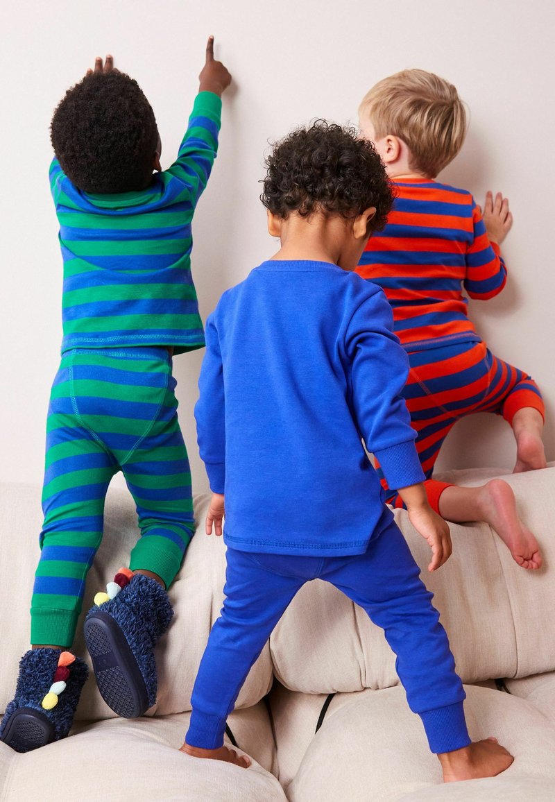 Tre børn i farverige pyjamaser: grønne og blå stribede toppe og bukser, ensfarvet blå top og bukser, rød og blå stribet top og orange bukser.