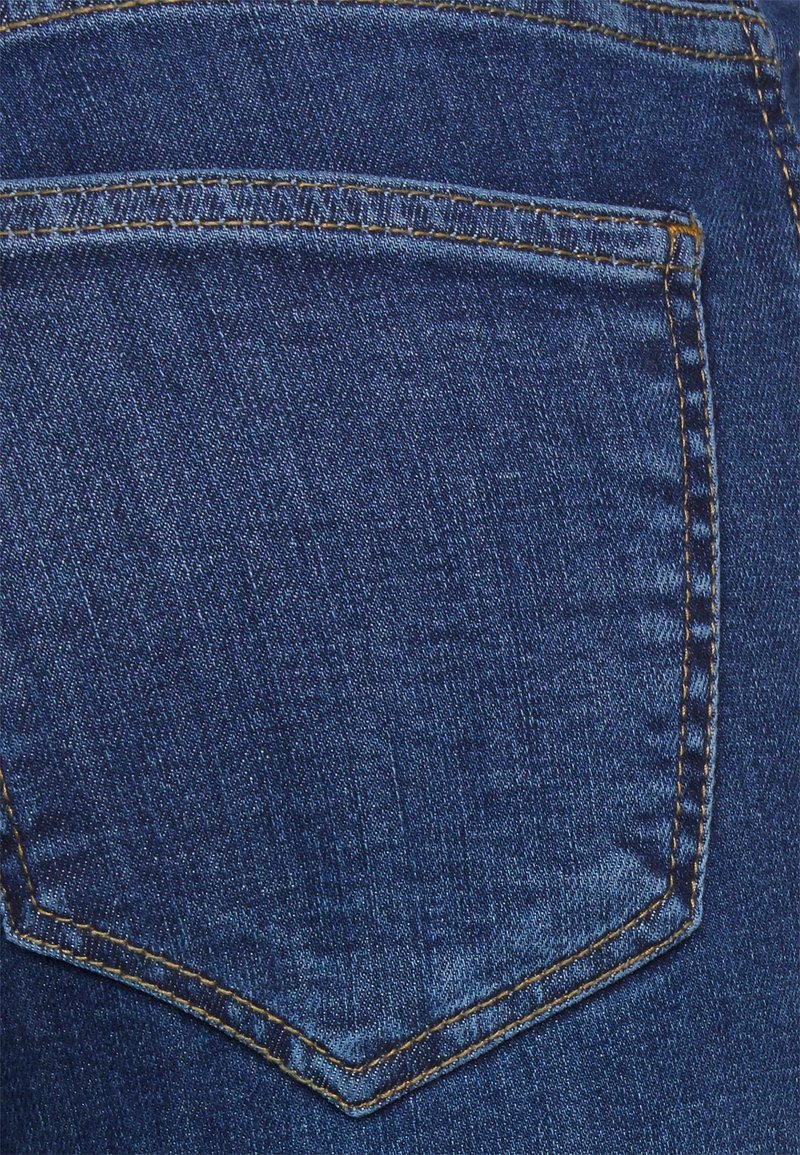 Primer plano de una tela de mezclilla azul con un bolsillo trasero cosido que presenta un detalle de hilo marrón dorado.