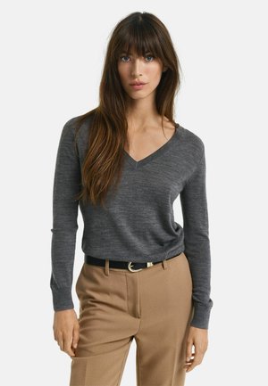 Grauer V-Ausschnitt-Pullover mit gestrickter Textur und langen Ärmeln, kombiniert mit braunen Hosen und einem schwarzen Gürtel mit einer silbernen Schnalle.