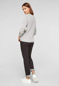 Pull en maille gris clair à manches longues, associé à un pantalon marron foncé retroussé et à des baskets blanches avec un accent argenté.
