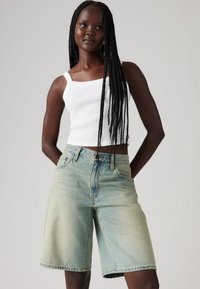 Svetlo modri jeans kratki hlače z visokim pasom in širokimi nogavicami, z kontrastnim šivanjem in sprednjimi žepi, v kombinaciji z belo majico brez rokavov.