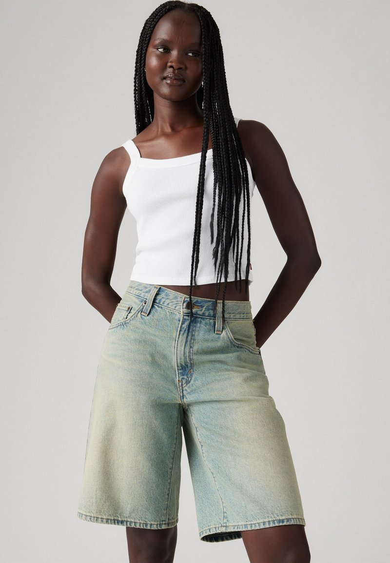 Svetlo modri jeans kratki hlače z visokim pasom in širokimi nogavicami, z kontrastnim šivanjem in sprednjimi žepi, v kombinaciji z belo majico brez rokavov.