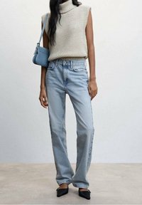 Suéter de punto crema sin mangas, jeans rectos de tiro medio en azul claro y bailarinas negras de punta, acompañado de un pequeño bolso de hombro azul.