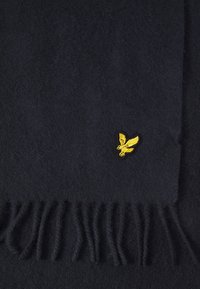 Tamno plava vuna šal s resicama na krajevima i malim žutim izvezenim logotipom orla blizu jednog ruba.