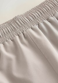 Ceinture élastique beige en tissu doux avec des lignes de couture visibles, montrant une texture froncée et un matériau lisse sous la ceinture.