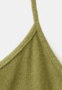 Gros plan sur un tissu en éponge vert olive avec une fine sangle et des surpiqûres texturées le long du bord triangulaire.