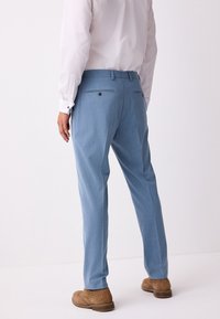 Hellblaue Anzughose mit maßgeschneiderter Passform, zwei Gesäßtaschen und glatter Textur. Kombiniert mit braunen Schuhen für ein elegantes Erscheinungsbild.