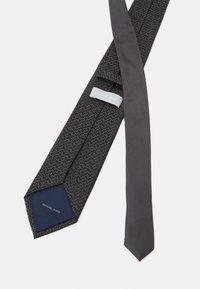 Cravat gri închis cu un model geometric și material texturat. Eticheta de pe spate citește "MICHAEL KORS." Capăt îngust cu un interior solid albastru.