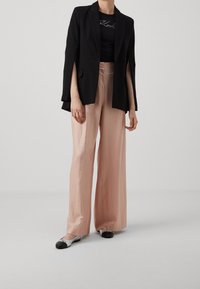 Blazer negro con mangas recortadas, combinado con una camiseta negra ajustada. Pantalones de pierna ancha en rosa claro y zapatos planos bicolor con detalles en negro y plateado.