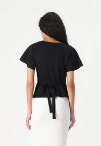 Čierny peplum top s krátkymi volánikovými rukávmi a viazaným pásom, v kombinácii s textúrovanou bielou sukňou. Hladká tkanina; neformálny dizajn.
