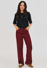 Čierny krátky rukáv top v kombinácii s červenými nohavicami s leopardím vzorom a širokými nohavicami. Mäkký materiál, vysoký pás a hladká textúra. Hnedé topánky.