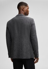 Schwarzer und weißer strukturierter Blazer mit einer klaren Form, Ein-Knopf-Schluss und Reverskragen, der ein dezentes Karomuster aufweist.