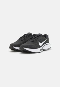 Un paio di scarpe da corsa Nike bianche e nere con design con lacci e suole imbottite, su uno sfondo chiaro e semplice.