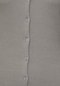 Cardigan cinza canelado com frente abotoada com botões transparentes e uma leve textura visível, exibindo um design ajustado.