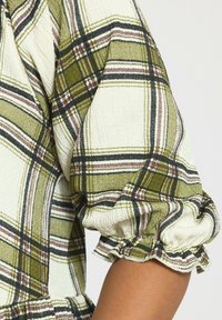 Blusa a maniche lunghe con un motivo a quadri bianco e verde, tessuto testurizzato e polsini elastici con bordo arricciato.