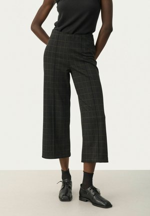 Pantaloni a vita alta a righe nere e verdi con un design a gamba larga. Tessuto liscio e silhouette sagomata, abbinati a scarpe nere.
