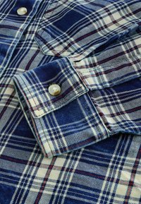 Blauwe en witte geruite flanellen shirt met mouwen, knoopmanchet en borstzak, met rode accentlijnen in het patroon.