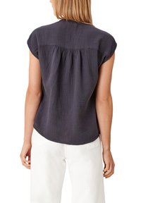 Haut gris foncé à manches courtes en tissu texturé avec un dos froncé. Ourlet arrondi et coupe décontractée, associé à un pantalon blanc.