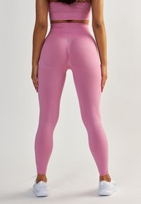Leggings rose taille haute avec une texture lisse, un design qui galbe les formes et des accents côtelés, associés à des chaussures de sport blanches.