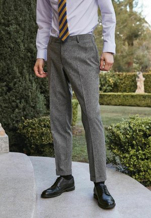 Pantalones de lana grises con un diseño entallado, combinados con una camisa de color azul claro y una corbata a rayas amarilla y azul, acompañados de zapatos de cuero negros.