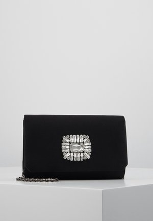 Czarna prostokątna kopertówka z srebrną ozdobą z kamieni i srebrnym łańcuszkowym paskiem, umieszczona na białej powierzchni na jednolitym szarym tle.