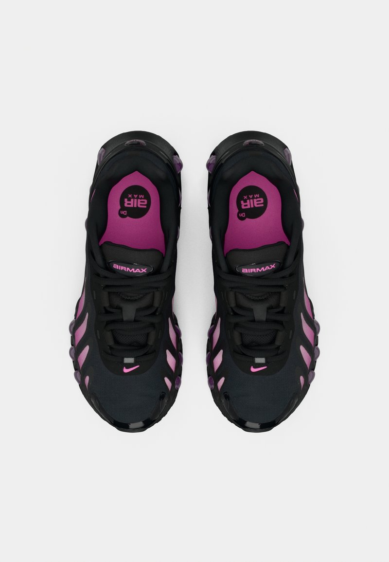 Schwarze Sportschuhe mit pinken Akzenten, ausgestattet mit einem strukturierten Obermaterial, sichtbaren Schnürsenkeln und einer gepolsterten Sohle mit einem auffälligen, gewellten Design.