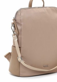 Zaino beige con un esterno in tessuto liscio, zip in metallo e spallaccio regolabile. Presenta una tasca laterale e un dettaglio con logo.