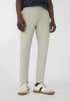 Chinos beige chiaro realizzati in un tessuto liscio, con un design affusolato. Abbinati a sneakers bianche con accenti grigi e neri.