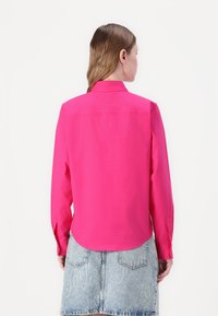 Fuchsia long-sleeve shirt with a collared neckline, button cuffs, and a structured design. Paired with a light blue denim skirt.