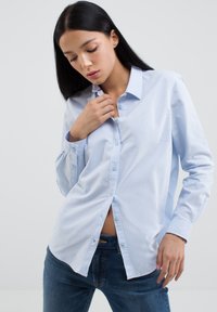 Camicia button-up in cotone azzurro chiaro con maniche lunghe, caratterizzata da una vestibilità comoda, una texture sottile e una piccola tasca sul petto.