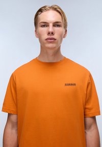 Orange bomulds t-shirt med rund hals, korte ærmer og et lille logo på venstre bryst. Glat tekstur og løstsiddende pasform.