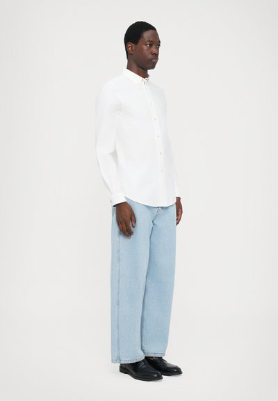 White button-up shirt with long sleeves and subtle texture; paired with light blue wide-leg jeans and black shoes.