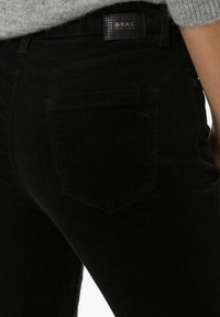 Black corduroy pants with a high waist, featuring a back pocket and a branded patch. The fabric has a pronounced ribbed texture.