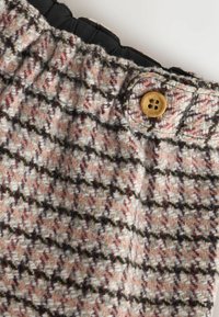 Uldstof i et lyserødt og beige houndstooth-mønster, med en sort elastisk talje og en rund træknaplukning.
