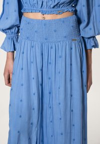 Lichtblauwe katoenen jurk met een smocked taille, geborduurde bloemenpatronen en pofmouwen. Bevat een klein metalen logo detail.
