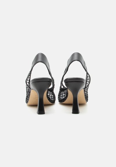 Mustad võrgust küljega ja nahkrihmadega slingback kontsakingad, vaadatuna tagantpoolt valge tausta ees.