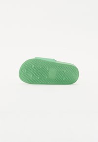 Grønn gummislipper såle med teksturert overflate, med sirkulære grep mønstre og en flat silhuett. Glatt øvre kant uten utsmykninger.