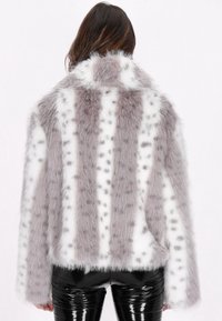 Faux fur jakke med skiftende grå og hvide striber, blød tekstur og plettede accenter, kombineret med skinnende sorte bukser.