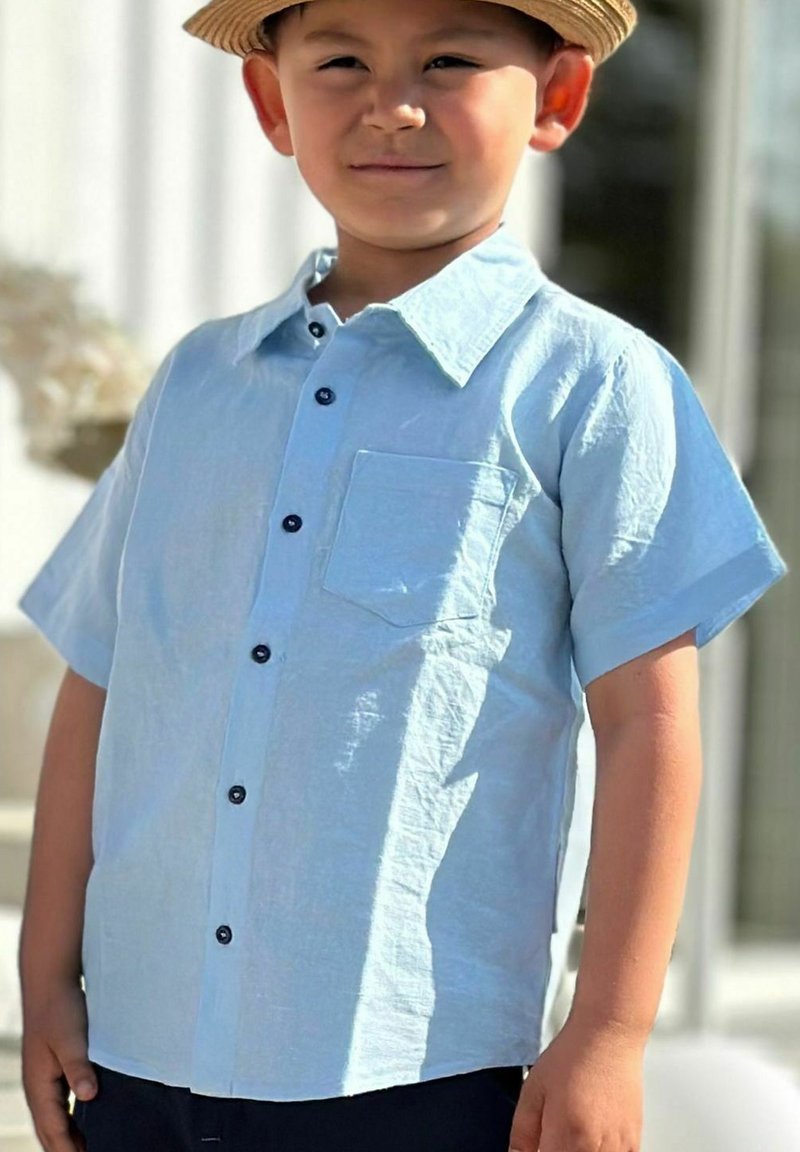 Vaaleansininen lyhythihainen paita nappikiinnityksellä, taskulla ja laivastonsinisin napein. Valmistettu teksturoidusta kankaasta, siinä on klassinen kaulustyyli.