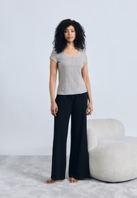 Γκρι κοντομάνικη μπλούζα με ριμπ υφή και στρογγυλή λαιμόκοψη, συνδυασμένη με μαύρο παντελόνι φαρδιάς γραμμής. Το μοντέλο στέκεται ξυπόλυτο σε απαλό γκρι χαλί.