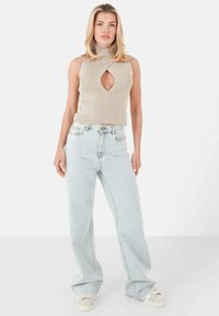 Top senza maniche a coste beige con un'apertura a chiave, abbinato a jeans azzurri a vita alta e gamba larga e sneaker beige.